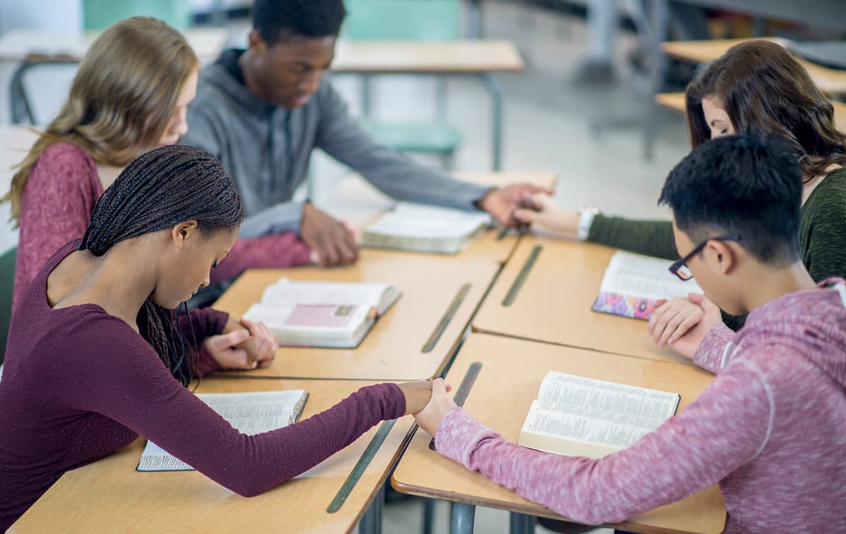 Young people gathered around a table during a faith discussion, reading and sharing together.